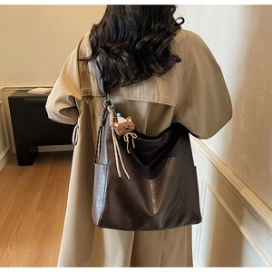 Détail du grand sac cabas marron foncé avec breloque ours en peluche sur un trench beige