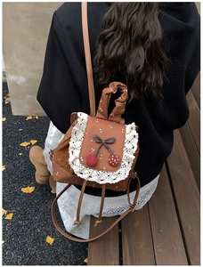 Gros plan d'un mini sac à dos vintage avec bordures en dentelle et breloques cerise
