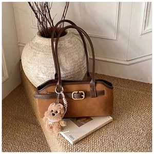 Makroaufnahme einer braunen Wildledertasche mit Lederriemen und süßem Teddybär-Anhänger
