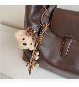 Detail of beige plush bear charm with leopard bow on a dark brown tote bag