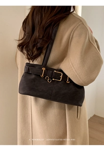 Close-up of matte black underarm bag with gold buckles on a wool coat model