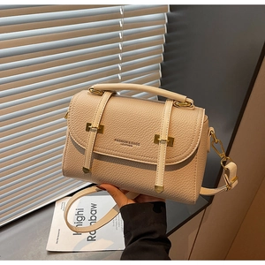 Detail of beige lychee grain leather crossbody bag with gold hardware and fashion lettering