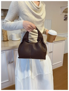 Sac seau en cuir marron foncé à motif litchi tenu par un mannequin dans une cuisine