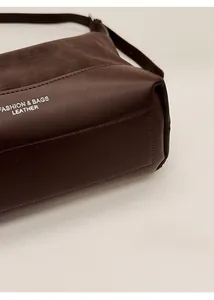 Close-up of precise stitching on the dark brown leather shoulder bag with structured base