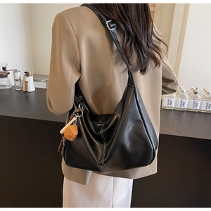 Detail of black leather tote bag featuring white contrast stitching and a small orange charm