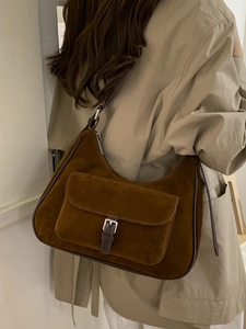 Brown suede half-moon tote bag with vintage buckle detail worn as a shoulder bag