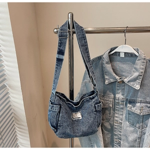 Detail of vintage washed denim crossbody bag featuring functional side pockets and wide strap