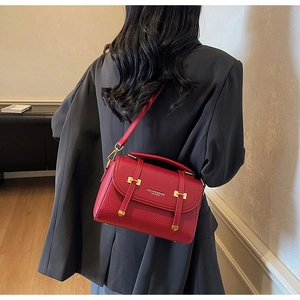 Detail of red pebbled leather satchel featuring gold buckle and crossbody strap detail