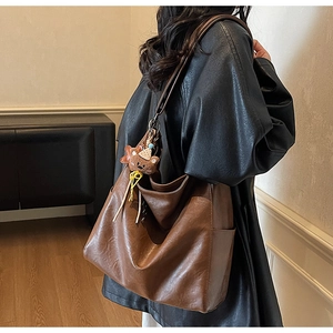 Brown leather tote bag detail with vintage texture and cute teddy bear plush charm