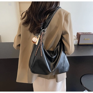 Détail du sac hobo en cuir mat noir avec coutures blanches et breloque baseball