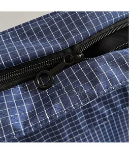 Detail showing the smooth black zipper and round metal slider on a blue checkered nylon bag