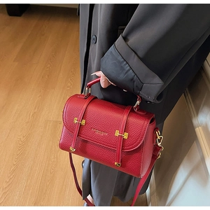 Detail of red lychee leather satchel with gold buckle and fashion text held by model