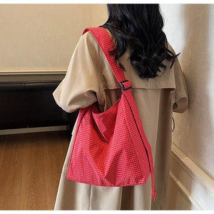 Detail of red and white plaid tote bag with adjustable black strap buckle on a model