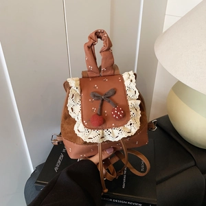 Détail d'un mini sac à dos vintage marron avec motif floral, dentelle et breloque cerise