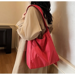 Close-up of red plaid canvas tote bag showing wide shoulder strap and fabric texture
