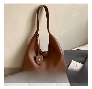 Detail of a brown lychee-grain leather hobo bag with a decorative heart-shaped pendant