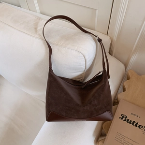 Close-up of brown suede and leather shoulder bag with adjustable strap on white sofa