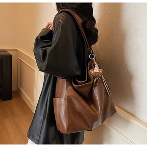 Detail of a brown leather tote bag with a bear charm, showing side pockets and texture