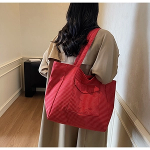 Close-up of red plaid tote bag with front pocket shown on a model in a trench coat