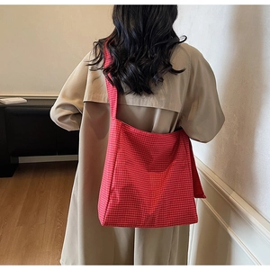 Detail shot of the large red checkered oxford tote bag worn by a model in a beige coat