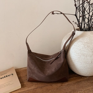 Detailed view of brown suede shoulder bag with leather reinforced corners on wood table