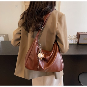 Détail du sac seau hobo en cuir caramel avec un pendentif de baseball décoratif unique