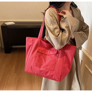 Detail of red checkered canvas tote bag with front pocket shown on a trench coat
