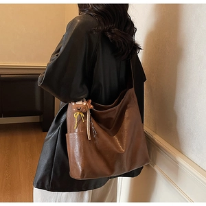 Detail of a brown leather shoulder bag featuring a cute teddy bear charm on the side pocket