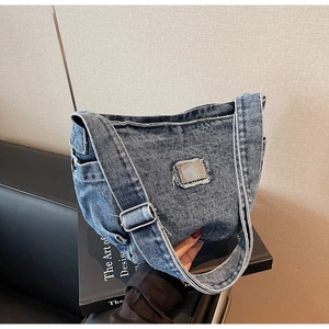 Détail rapproché du sac d'épaule en denim bleu clair avec plaque métallique rectangulaire