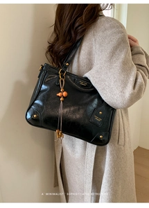 Macro shot of black glossy leather tote bag with gold hardware and vintage bead tassel