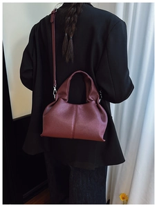 Gros plan du sac seau en cuir bordeaux à motif litchi avec plis nuages et bandoulière