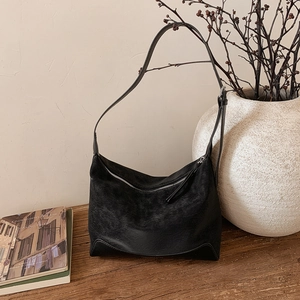 Detail of a vintage black suede shoulder bag with leather base on a rustic wooden table