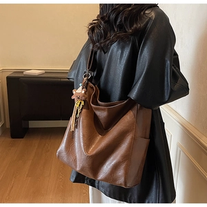 Brown faux leather hobo bag with teddy bear charm shown worn on a model shoulder