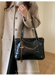 Detail of a black leather tote bag with gold logo and orange tassel on a beige coat