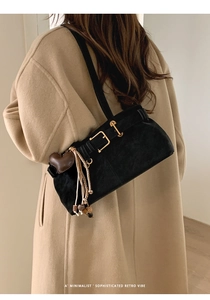 Detail of black matte underarm bag with gold buckle and brown heart pendant on camel coat