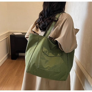 Close-up of green checkered canvas tote bag with wide shoulder strap and large front pocket