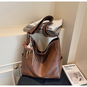 Detail of dark brown faux leather tote bag with a small bear pendant charm side pocket