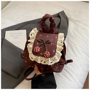 Détail du mini sac à dos marron vintage avec dentelle blanche et nœud cerise brodé