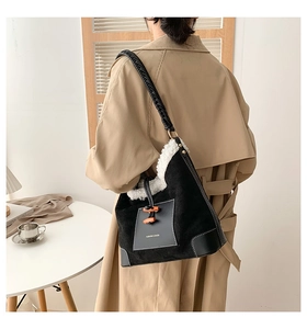 Detail of plush black suede shoulder bag featuring orange horn buckles and woven strap