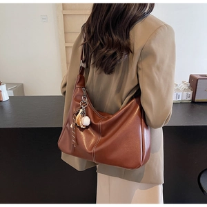 Brown soft leather hobo bag with white stitching and baseball glove charm worn by a model