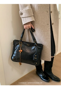 Detail of black vintage leather tote bag with gold hardware and orange bead charm