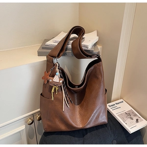 Brown leather hobo tote bag with a bear charm accessory in a warm interior setting