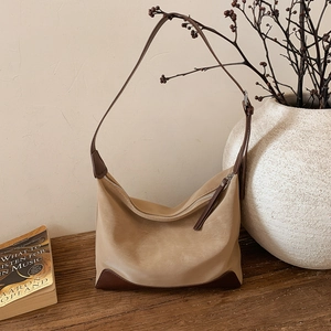 Close-up detail of khaki hobo bag with dark brown trim on a textured wooden surface