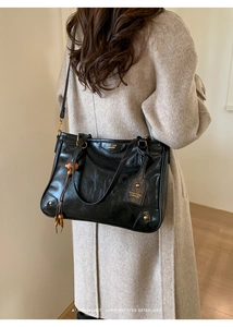 Detail of black vintage leather tote bag with gold lettering and tassel charm accessory