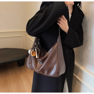 Detail view of brown leather hobo bag with white stitching and baseball bag charm