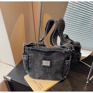 Gros plan du sac bandoulière en denim foncé avec plaque métallique et poches latérales