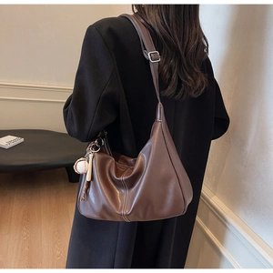 Detail of dark brown leather hobo bag with white stitching and baseball bat charm