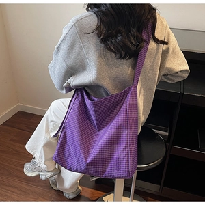 Detail of a large purple plaid oxford tote bag worn by a model in a casual indoor setting