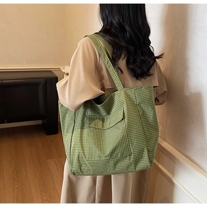 Detail of green plaid tote bag with front pocket carried by a model in beige trench coat