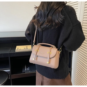 Rear view of a model wearing a taupe pebble leather messenger bag with gold hardware